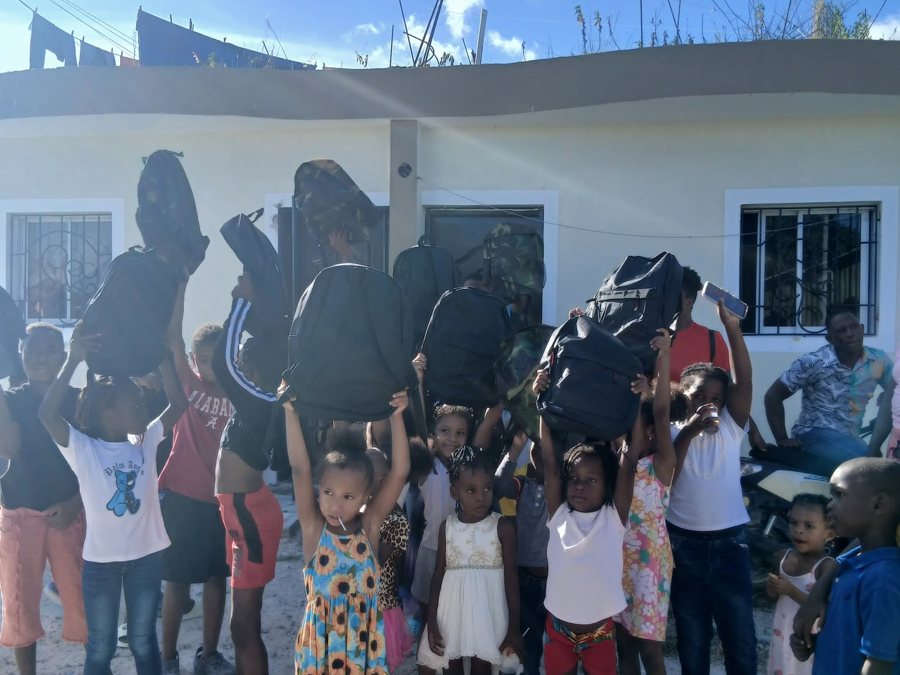 Niños y niñas levantando sus mochilas nuevas frente a una casa