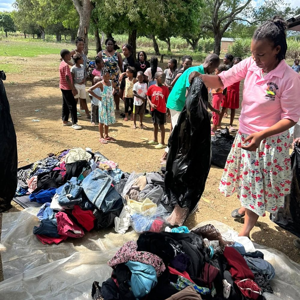 Voluntaria de la fundación repartiendo ropa a las familias bajo los árboles