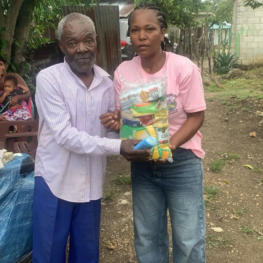 Voluntaria entregando una funda de alimentos a un señor mayor
